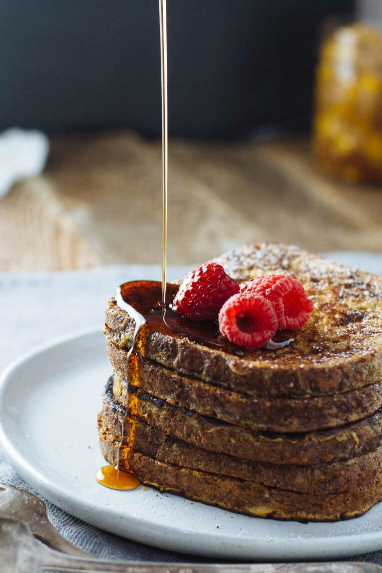 The most delicious Healthy French Toast made with simple ingredients including Ezekiel bread which is packed with healthy grains. This recipe is super easy to whip up and is perfect for lazy weekend breakfast or brunch with a side of eggs and hot cup of coffee. #healthyfrenchtoast #frenchtoast A stack of healthy French Toast on a plate with syrup getting poured over