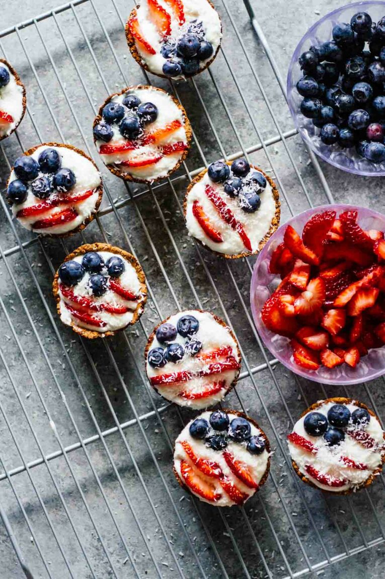 The cutest little Fruit Tarts made with blueberries and strawberries, perfect for Fourth of July! These patriotic tarts not only look the part but they taste incredible and better yet they're super healthy! #fruittarts #berrytarts Patriotic Mini Fruit Tarts on a cooling rack with berries