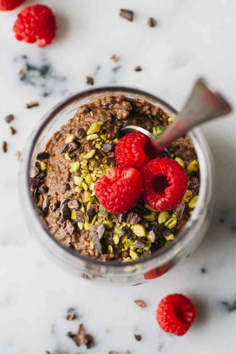 Overhead shot of Vegan Chocolate Chia Seed Pudding in a glass cup and topped with raspberries, pistachios, and cacao nibs!