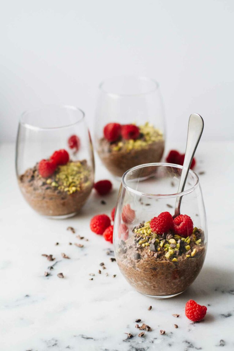 Three cups of Vegan Chocolate Chia Seed Pudding topped with raspberries, pistachios, and cacao nibs!