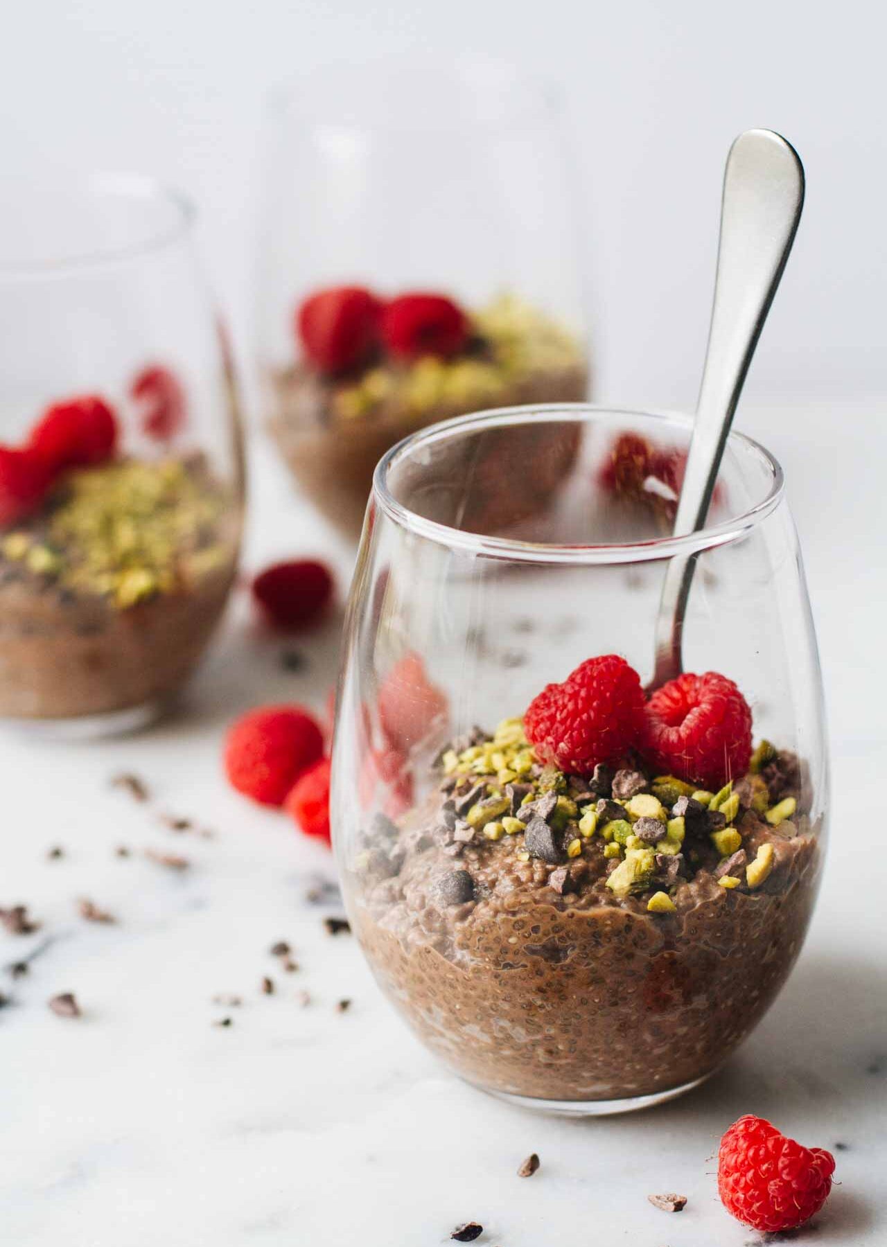 Vegan Chocolate Chia Seed Pudding in a glass cup and topped with raspberries, pistachios, and cacao nibs!