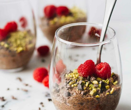 Vegan Chocolate Chia Seed Pudding in a glass cup and topped with raspberries, pistachios, and cacao nibs!