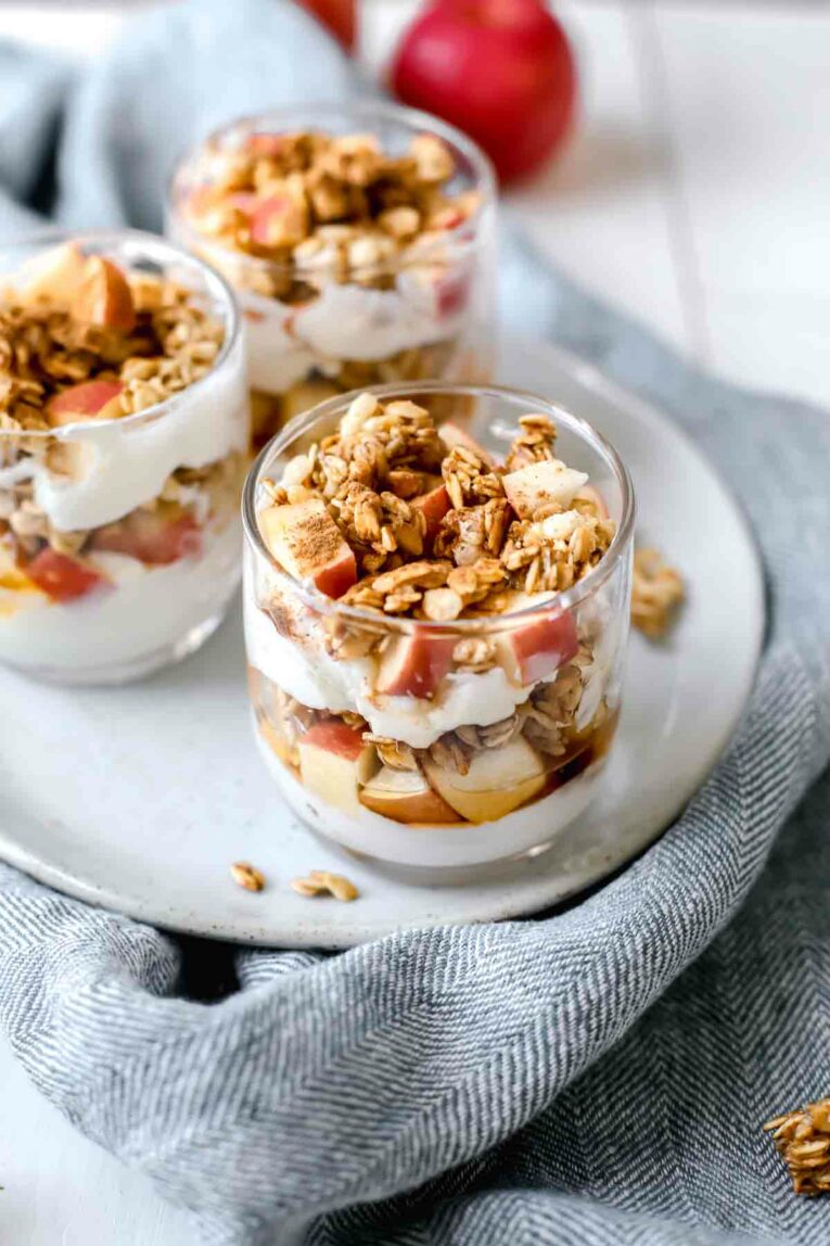Apple Crumble Parfaits in 3 glass cups on a grey plate over a linen napkin.
