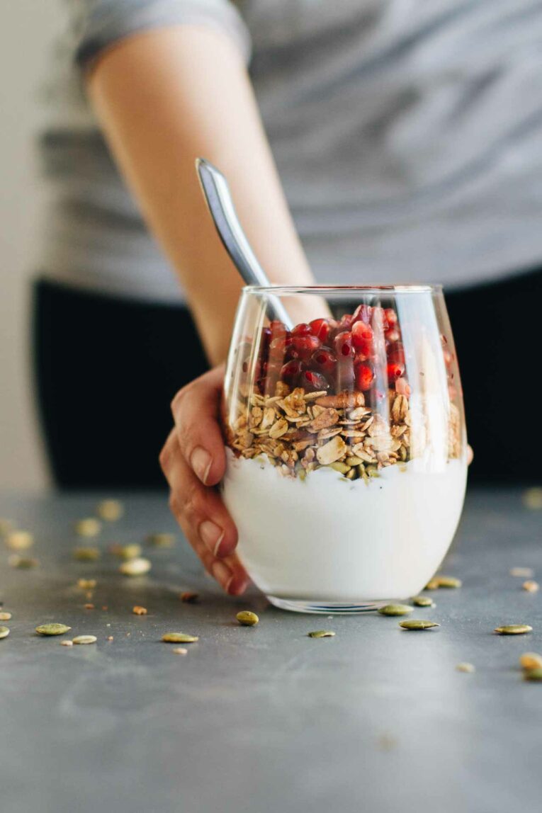 Hand holding Pomegranate Breakfast Parfait in a glass with a spoon
