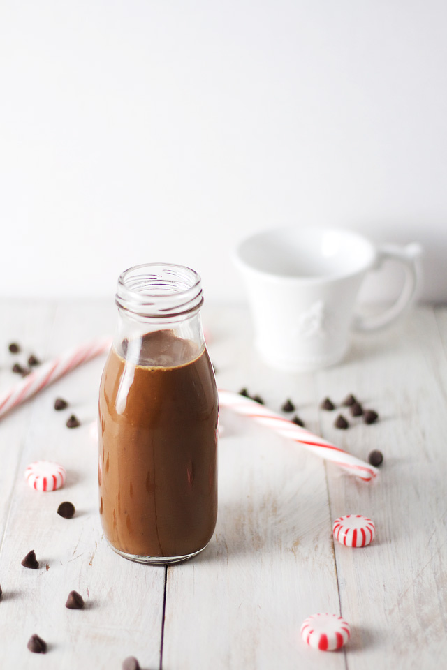 A Skinny Iced Peppermint Mocha in a glass milk bottle with candy canes and chocolate chips beside it
