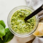 A jar of spinach pesto with a spoon coming out of the top of it.