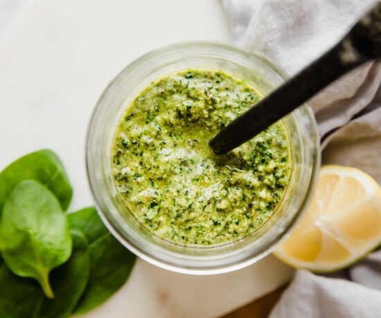 A jar of spinach pesto with a spoon coming out of the top of it.