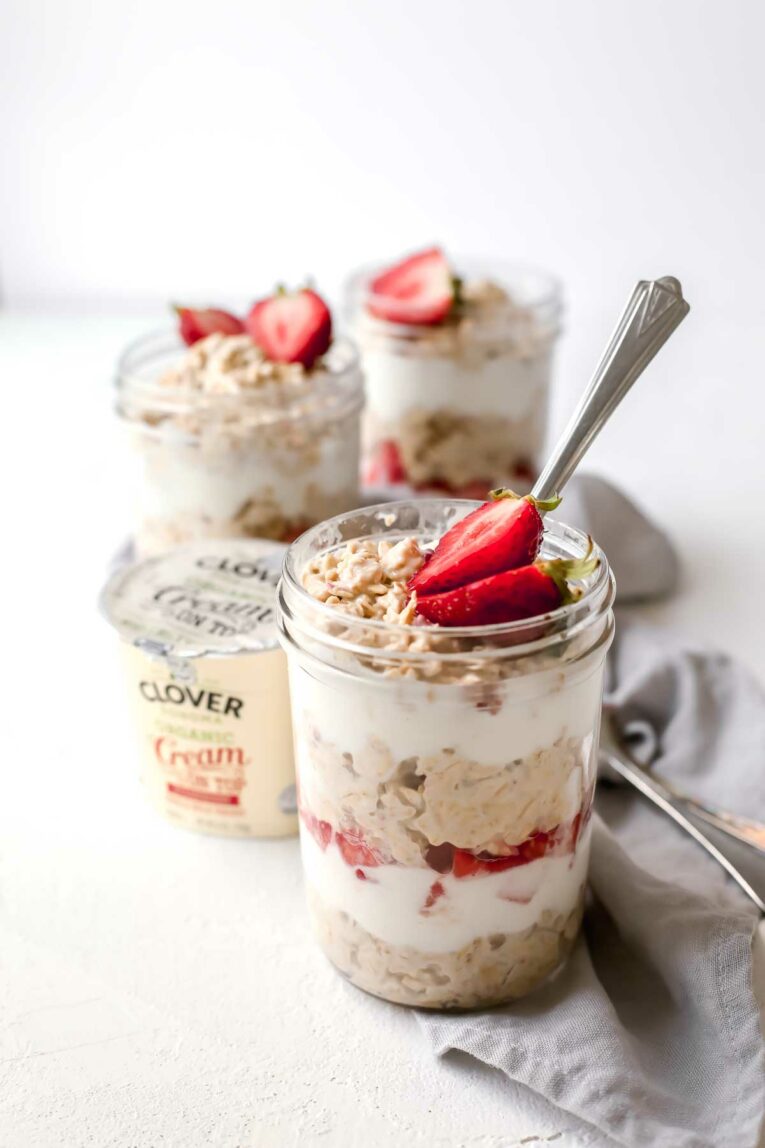 Strawberries & Cream Overnight Oats served in mason jars with a spoon next to clover yogurt.