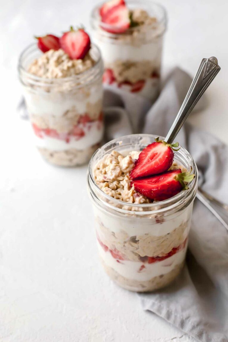 Strawberries & Cream Overnight Oats served in 3 mason jars with a spoon.
