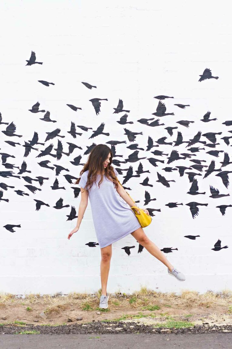 girl standing in front a white building with black birds painted on it