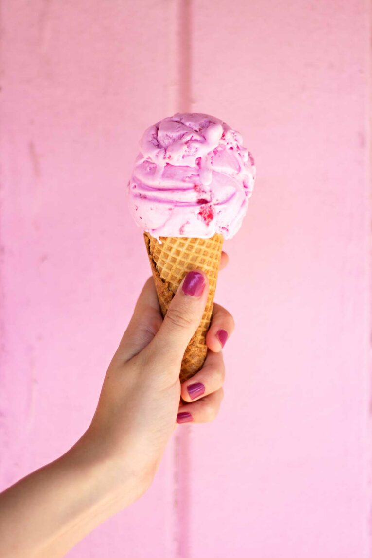 someone holding pink ice cream cone in front of pink background
