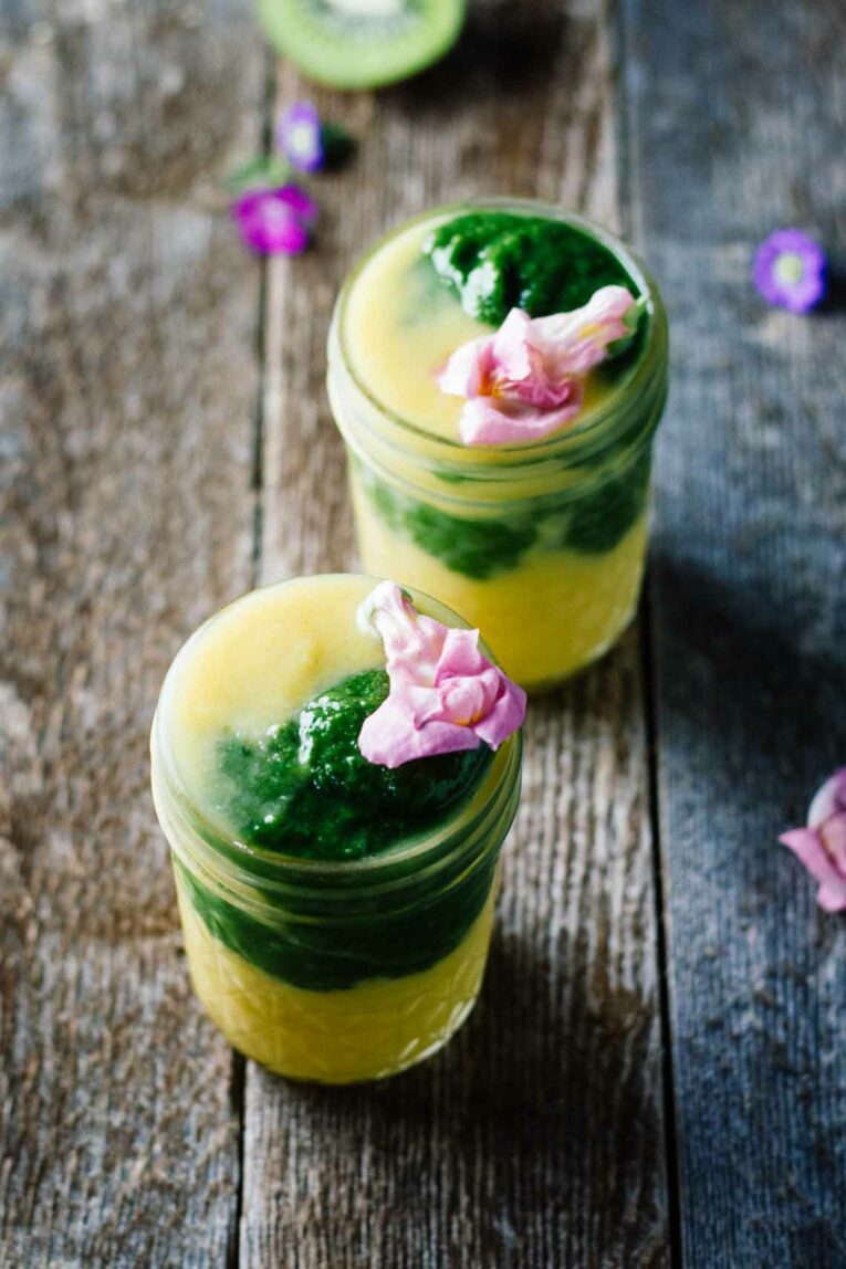 Two turmeric smoothies in mason jars topped with flowers