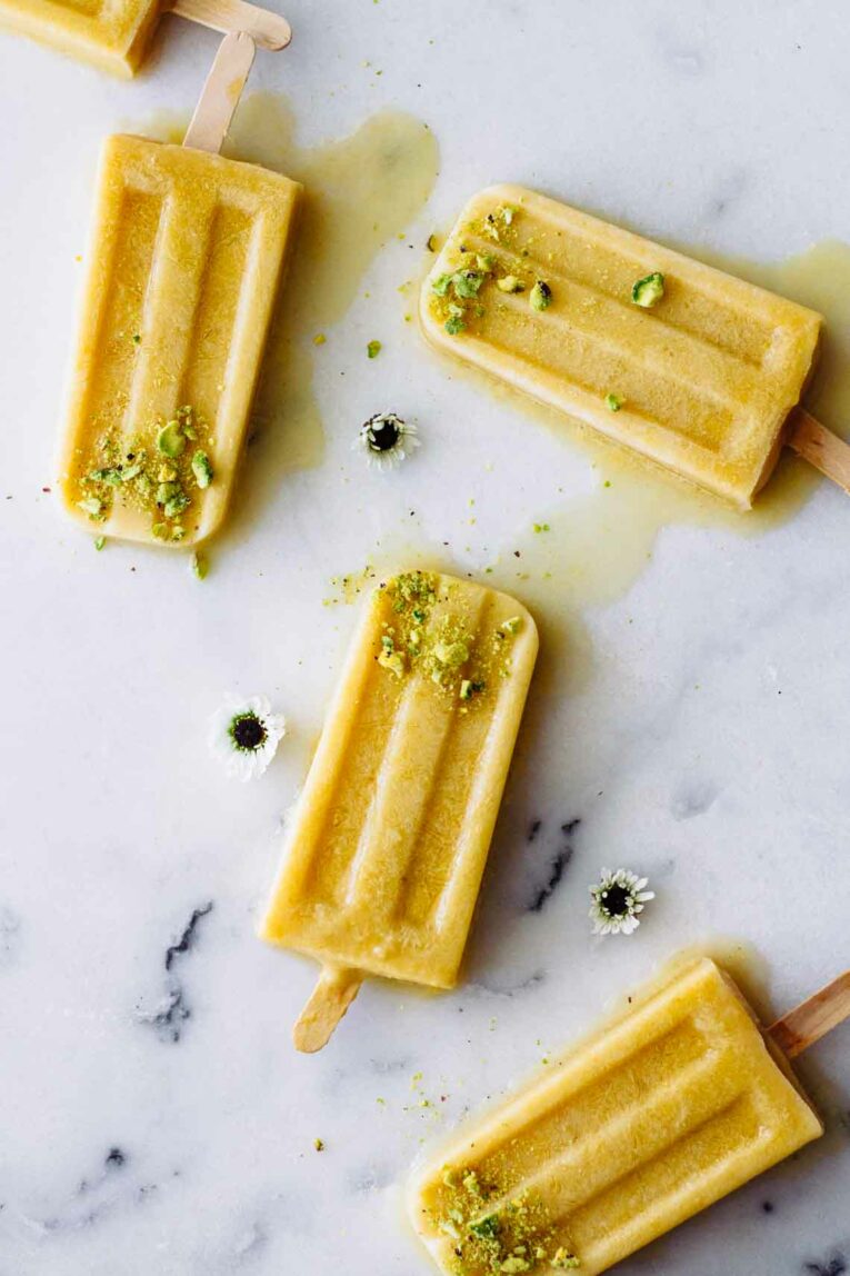 Coconut Peach Turmeric Popsicles slightly melting scattered on a marble counter