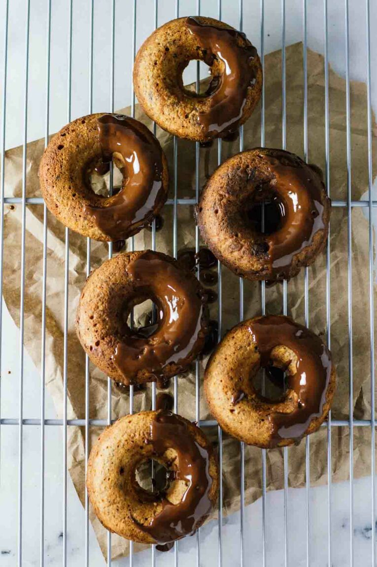The easiest healthy donuts with peanut butter and chocolate that are made in a blender. These chocolate treats are not only super easy to whip up but they are healthy too! Get your chocolate donut fix minus the guilt and in only 25 minutes! #jaroflemons #donuts #healthydonuts An overhead shot of healthy donuts with Peanut and Butter Chocolate on a blue cooling rack
