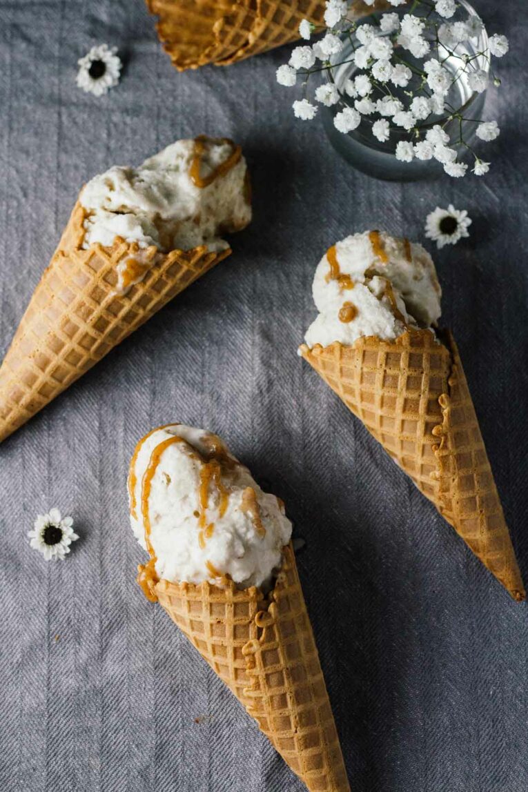 Vegan Salted Caramel & Chamomile Ice Cream in waffle cones laying on a grey surface with flowers on the side