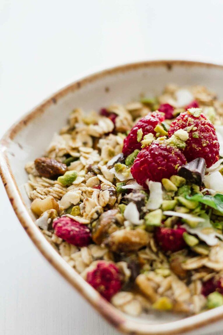 Homemade Chocolate Raspberry Muesli! Vegetarian, gluten-free, refined sugar free. An easy, quick, and healthy breakfast! Make this stuff in about 10 minutes and keep it in your pantry for 2 or more weeks! #Jaroflemons #Muesli #healthybreakfast A close up of a bowl of homemade muesli topped with raspberries and pistachios