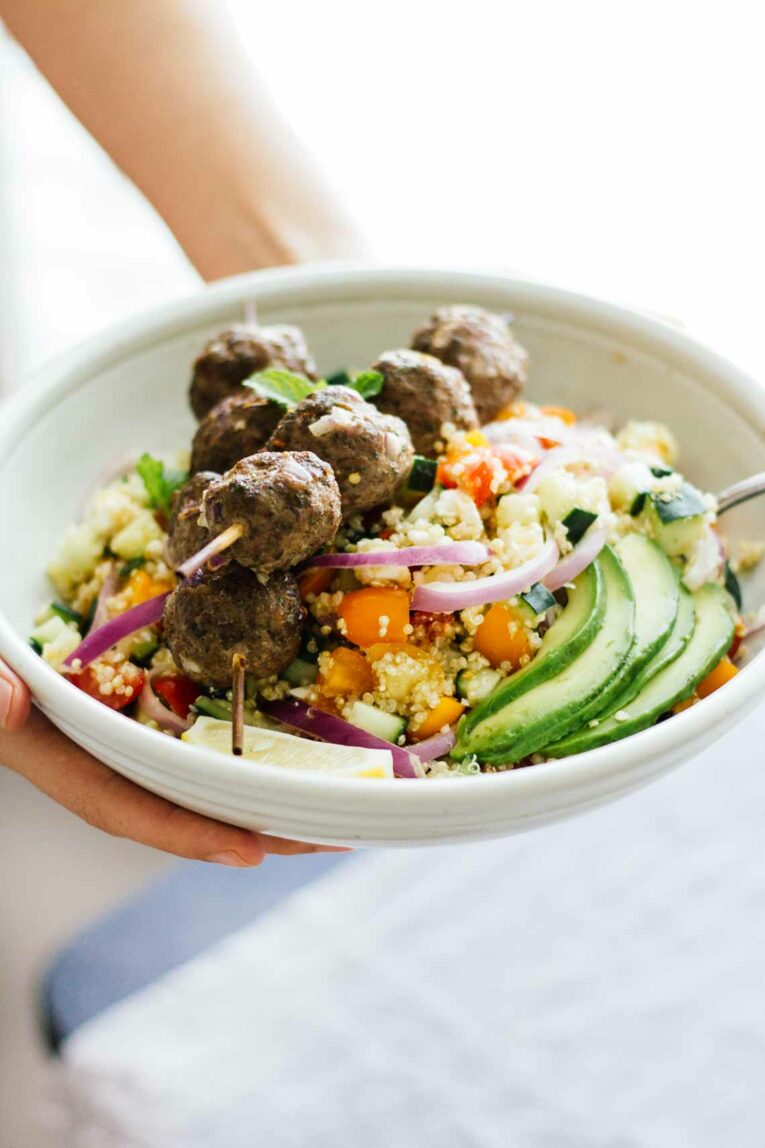 Hand holding bowl of Mediterranean Salad Bowls w/ Lebanese BBQ Meatballs