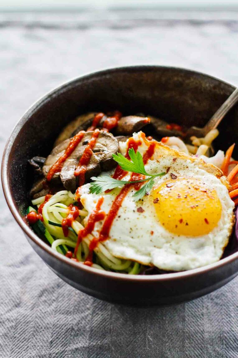 Side view of Vegetarian Spicy Korean Bibimbap Bowls with a grey background