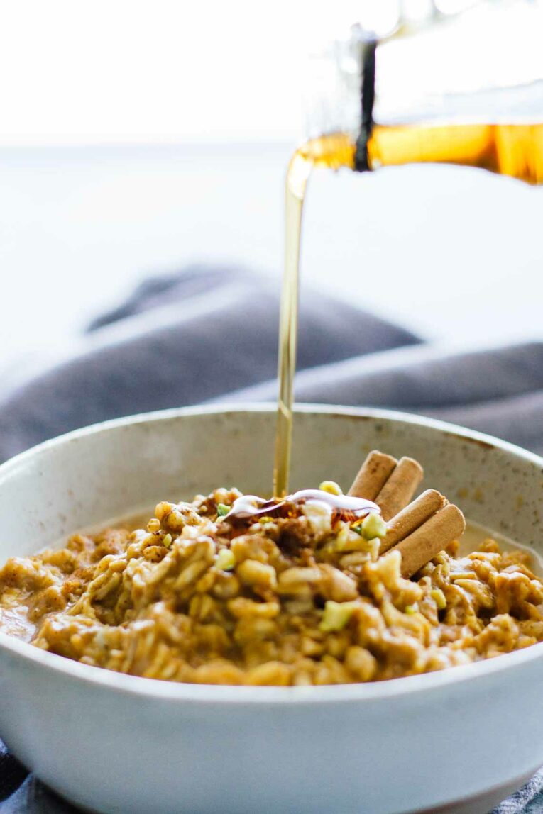 A side shot of Pumpkin Oatmeal in a bowl with syrup getting poured over