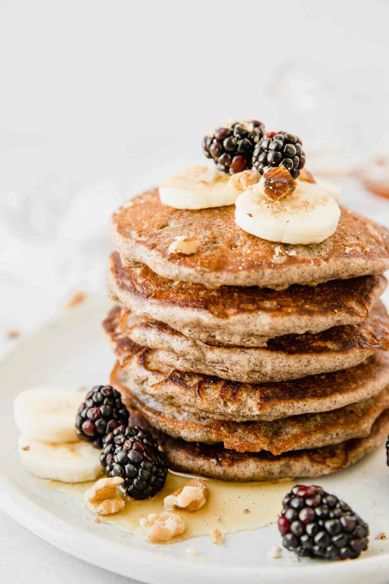 Buckwheat Pancakes on a white plate with syrup and berries.