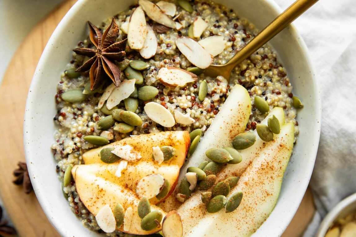 Breakfast Quinoa in a Bowl Topped with Sliced Almonds, Pumpkin Seeds, Cinnamon, and Apple Slices