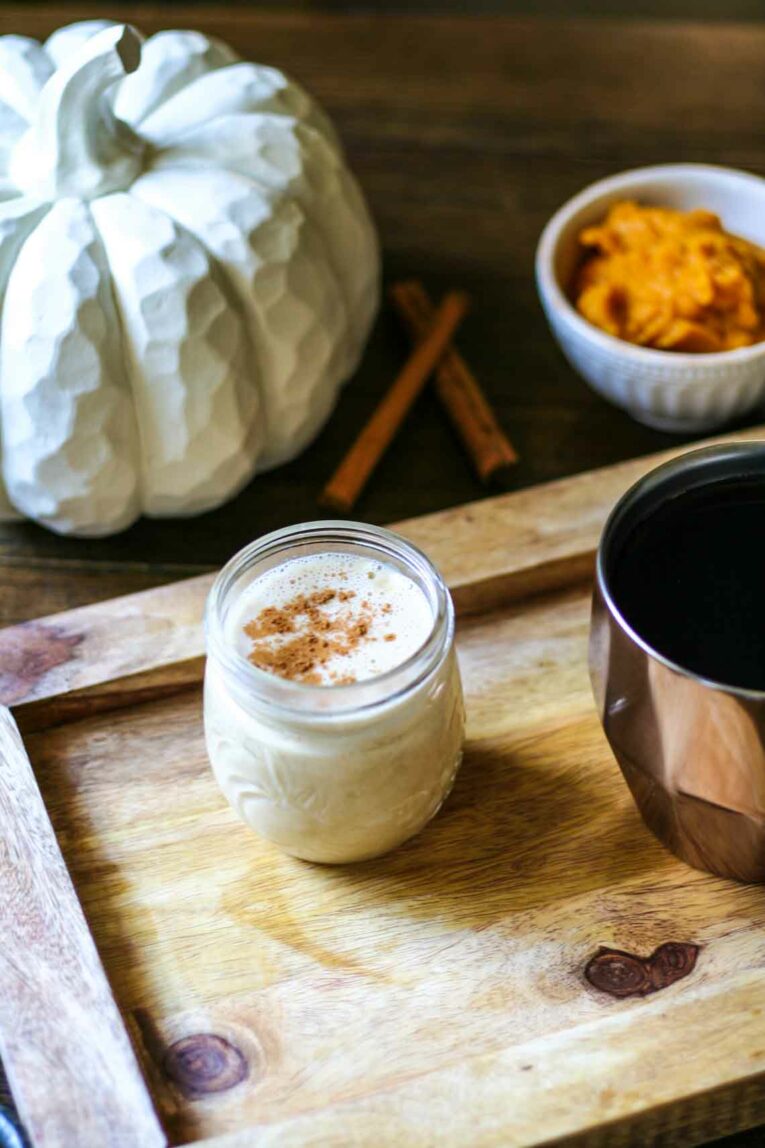 Paleo Pumpkin Coffee Creamer in a glass jar next to a decorative pumpkin, cinnamon sticks, and pumpkin puree