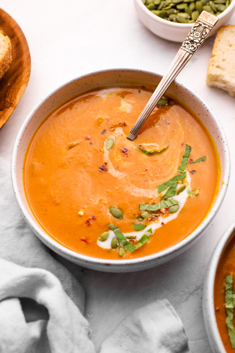 Pumpkin Curry Soup with a Yogurt Drizzle and Chopped Spinach in a White Bowl