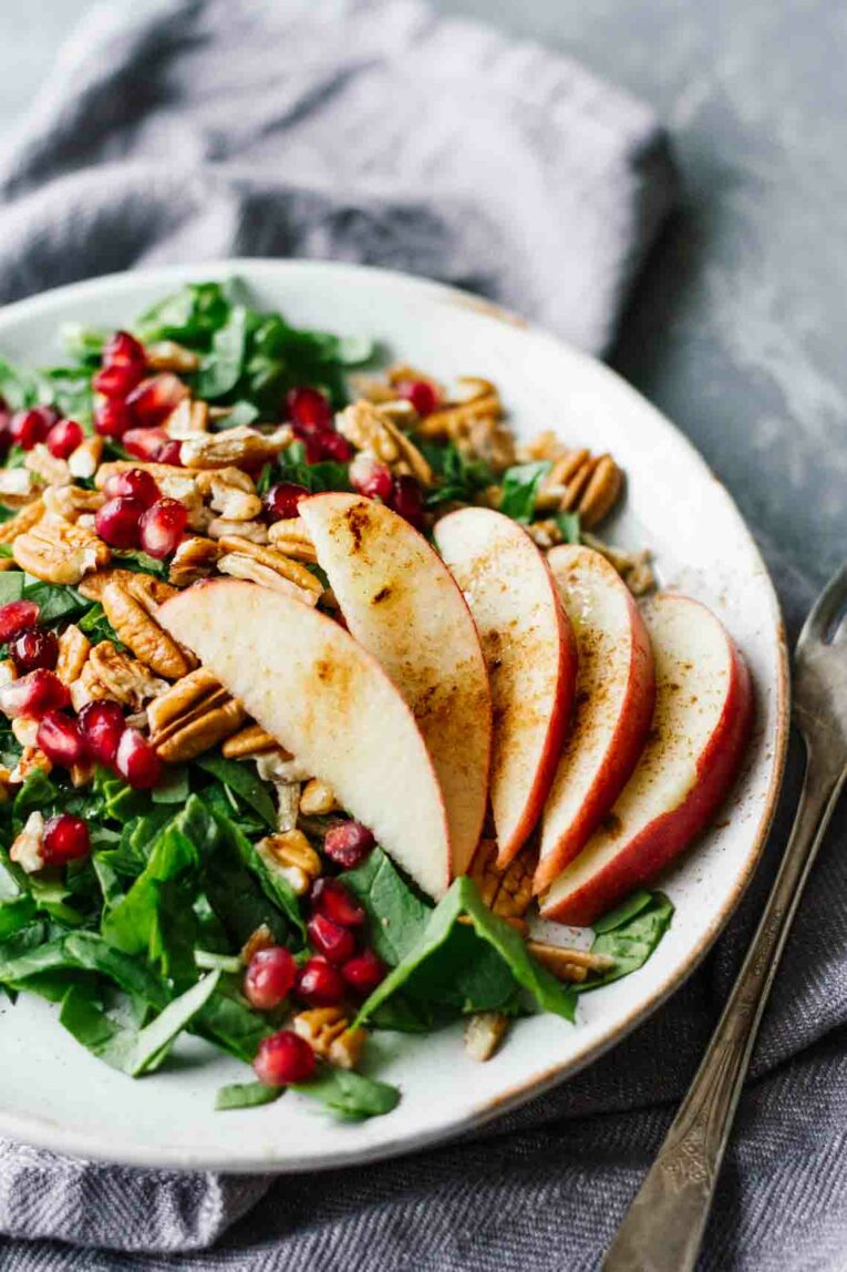 Pomegranate Pecan Salad w/ Cinnamon Apples served on a white plate next to fork