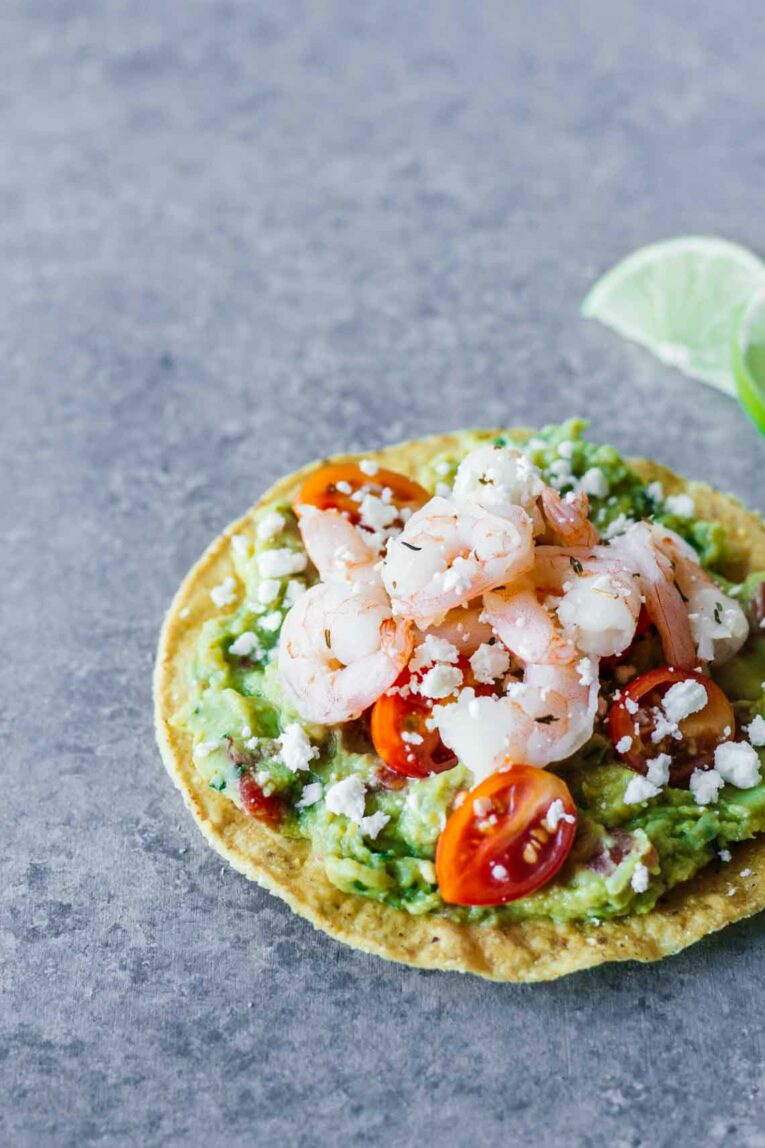 Shrimp Guacamole Tostada on grey surface next to lime wedge