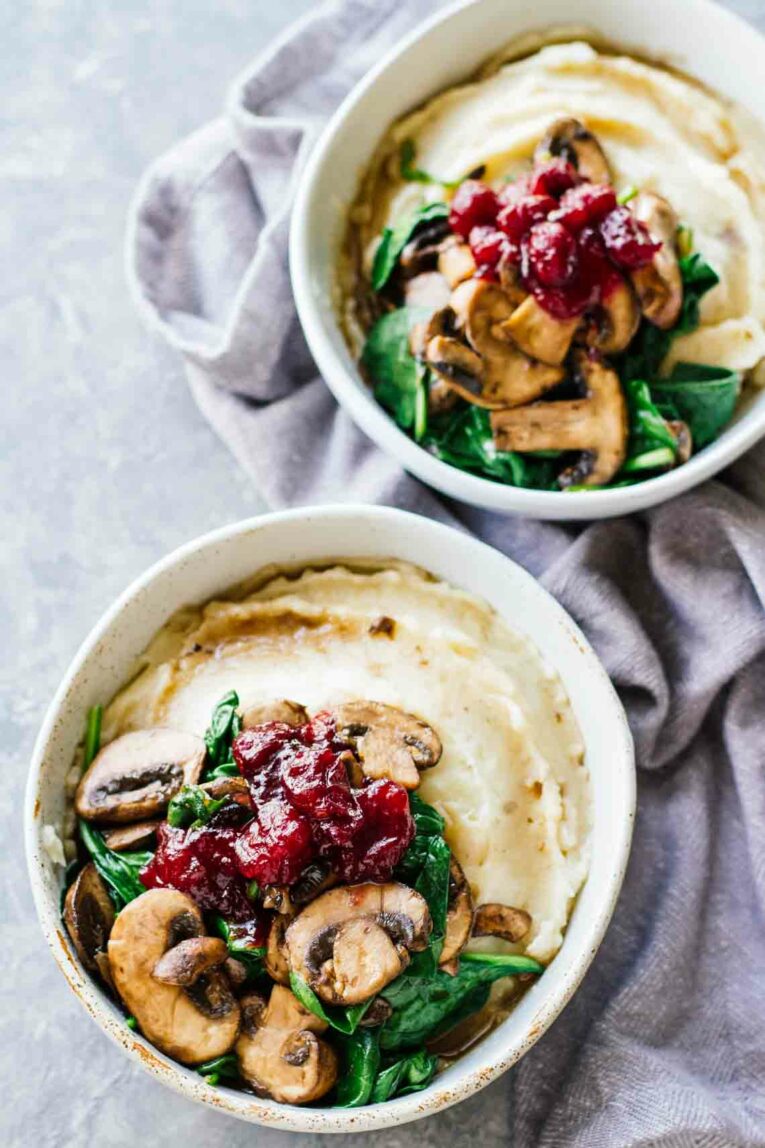 Slow Cooker Mashed Potatoes & Cranberry Mushroom Sauce in two white bowls sitting on a dishcloth