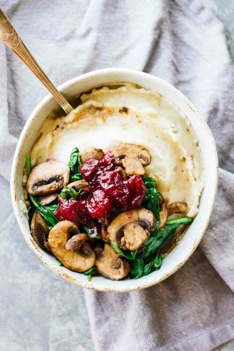 Slow Cooker Mashed Potatoes with Cranberry Mushroom Sauce and Spinach in a White Bowl