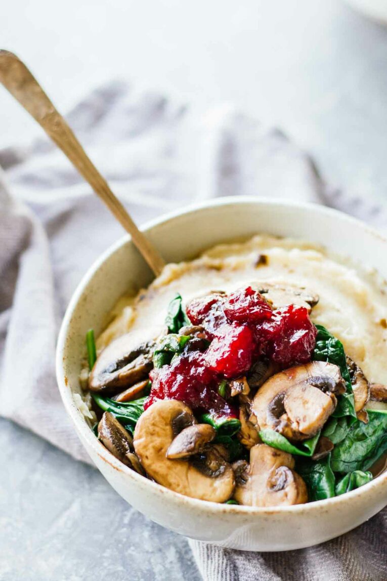Slow Cooker Mashed Potatoes & Cranberry Mushroom Sauce in a white bowl with a spoon