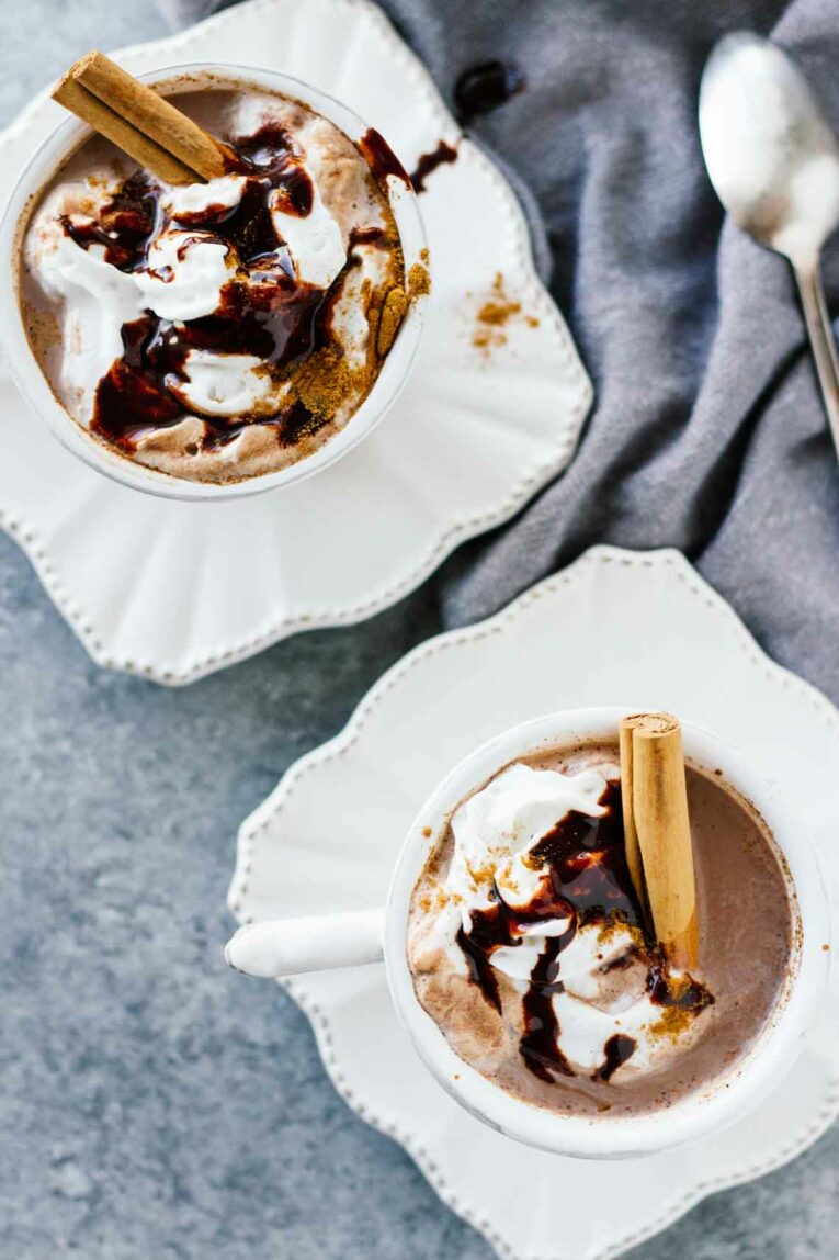 overhead shot of Slow Cooker Mexican Hot Chocolate served in white teacups with whipped cream and a cinnamon stick 
