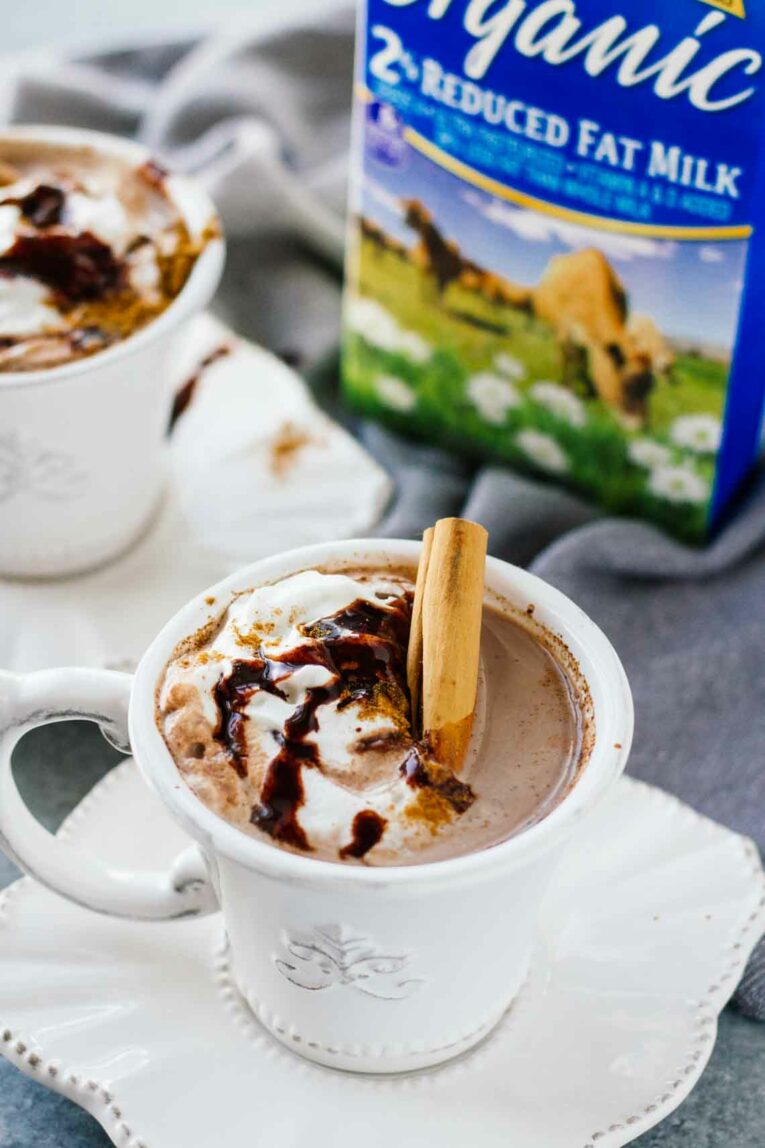 Slow Cooker Mexican Hot Chocolate in a white teacup with whipped cream and a cinnamon stick