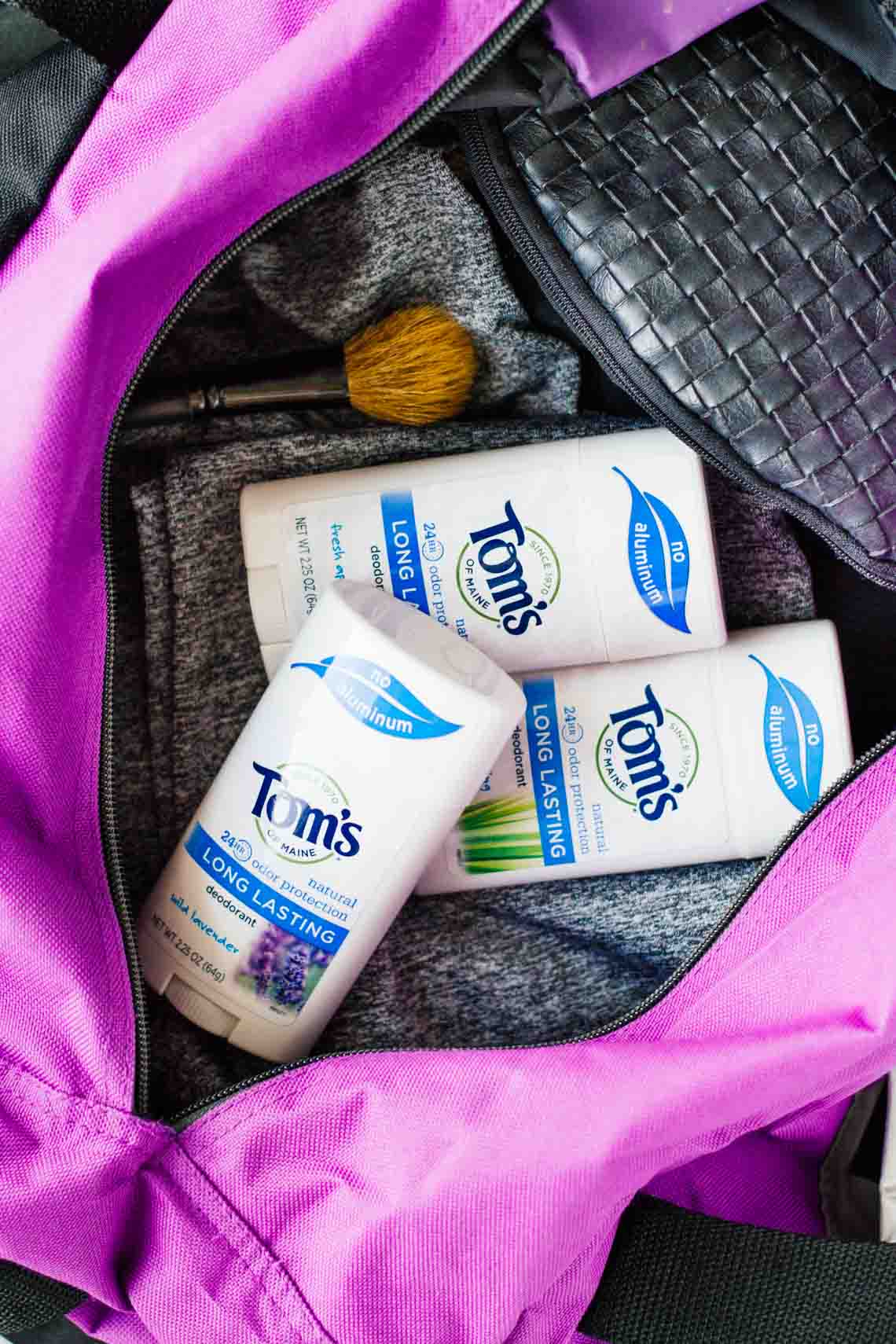 close up of Tom's deodorant laying inside a gym back with clothe sand makupbrush