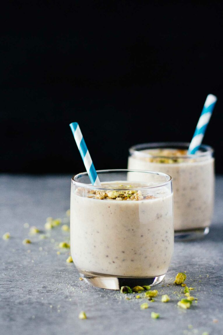 Two glasses of Chia Seed Smoothie sitting on a blue worktop with blue straws