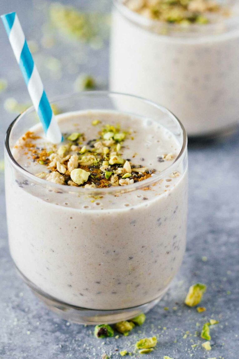 A close up of a Banana Cashew Butter Chia Seed Smoothie topped with nuts and a straw