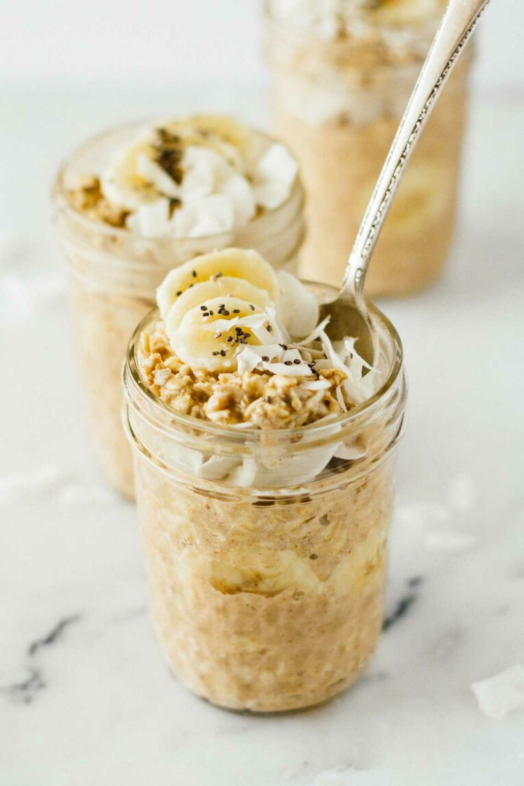 Banana Coconut Cream Pie Overnight Oats in a mason jar with a spoon.