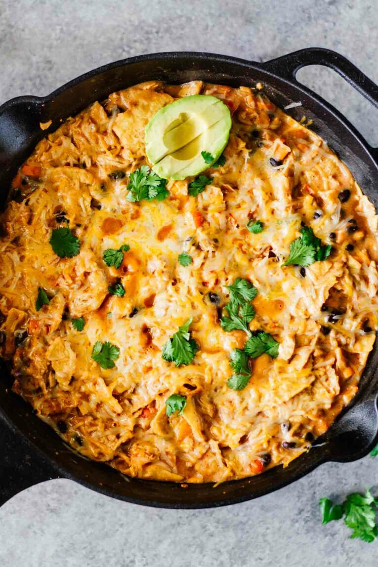 Creamy Healthy Chicken Enchilada casserole in a skillet topped with avocado and fresh cilantro.