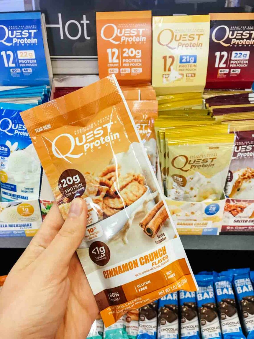 EASY Cinnamon Crunch Protein Bites! Super easy to make, 10 minutes, and loaded with protein. Delicious! #proteinbites #proteinballs A hand holding a packet of Quest protein powder in a supermarket