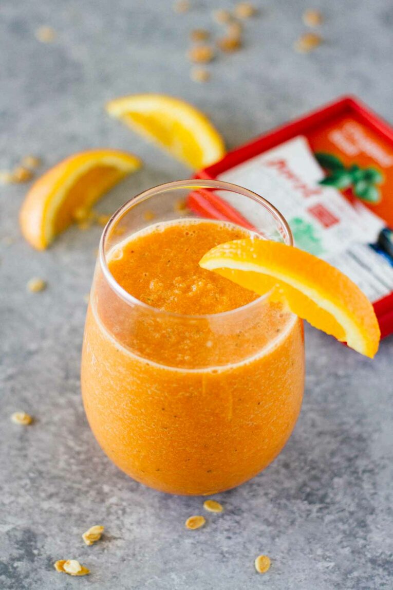An overhead shot of an orange carrot smoothie in a glass with wedges or orange