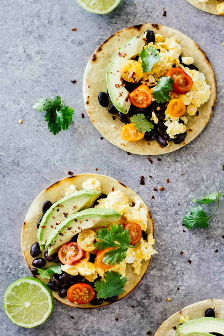 An overhead shot of two breakfast tacos with avocado and lime