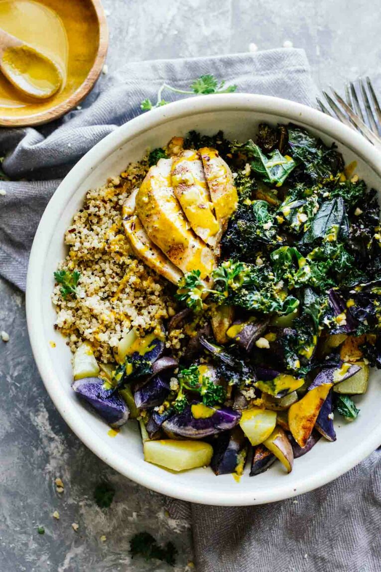 Baked Chicken with Quinoa, Kale, Potatoes, and Turmeric Sauce in a White Bowl