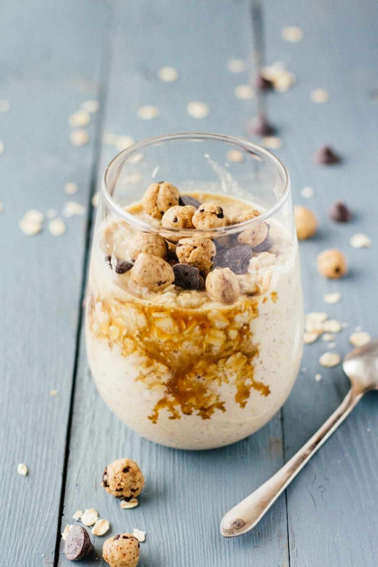 Chocolate Chip Cookie Dough Overnight Oats in a glass on a wooden surface next to a spoon.