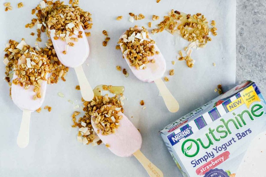 An overhead shot of strawberry frozen yogurt bars on baking parchment with granola and honey