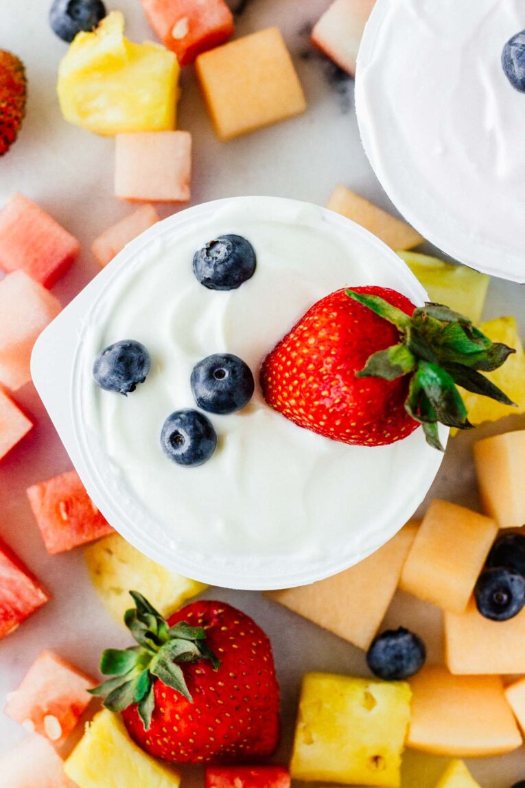 overhead shot of yogurt in a cup with berries on top surrounded by fruit