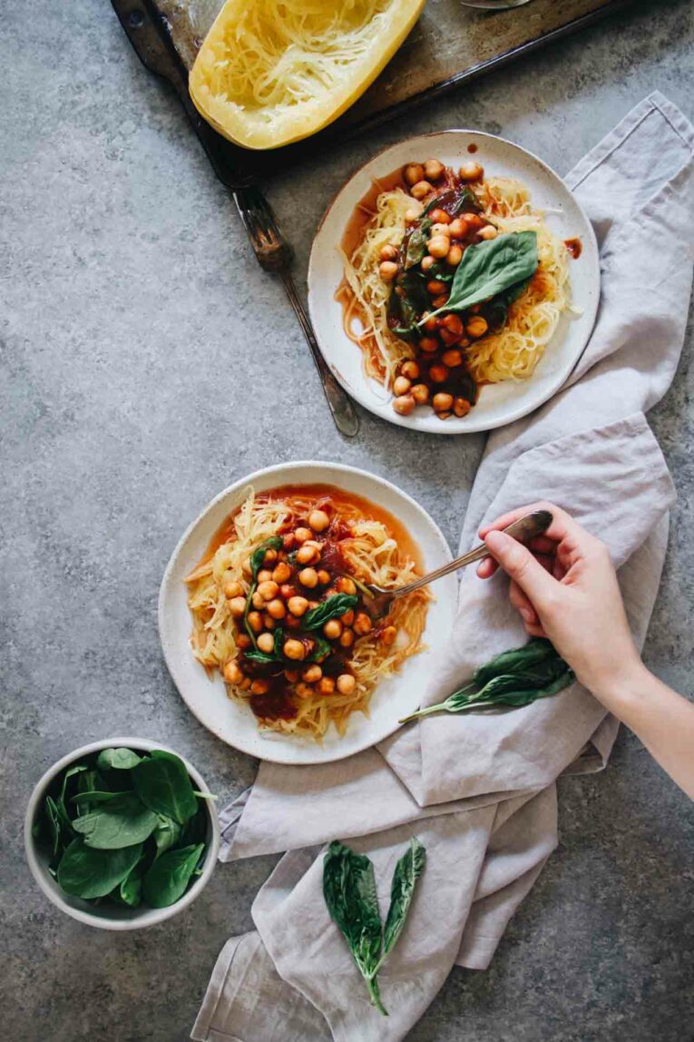 Overhead shot of Garlic Chickpea Spaghetti Squash served on two plates with a hand holding a fork