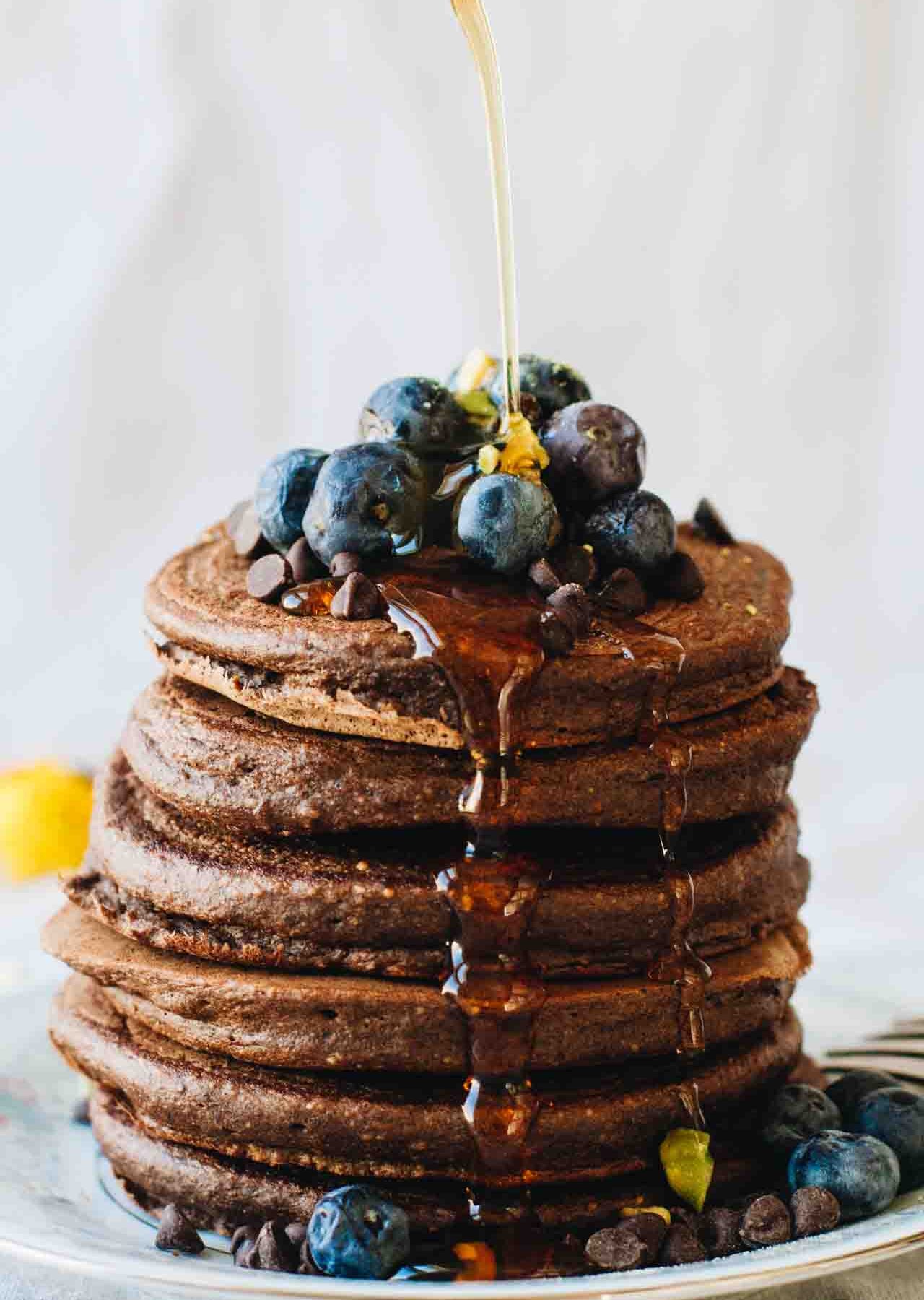Chocolate Protein Pancakes with blueberries and syrup pouring over them! Loaded with superfoods, protein, fruit, eggs, and rolled oats. They also happen to be gluten and dairy free!