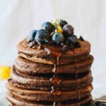 Chocolate Protein Pancakes with blueberries and syrup pouring over them! Loaded with superfoods, protein, fruit, eggs, and rolled oats. They also happen to be gluten and dairy free!