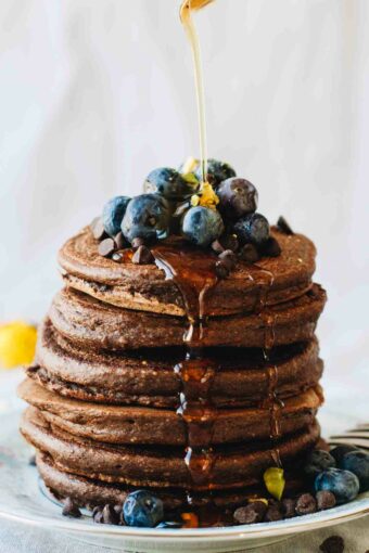 Chocolate Protein Pancakes with blueberries and syrup pouring over them! Loaded with superfoods, protein, fruit, eggs, and rolled oats. They also happen to be gluten and dairy free!